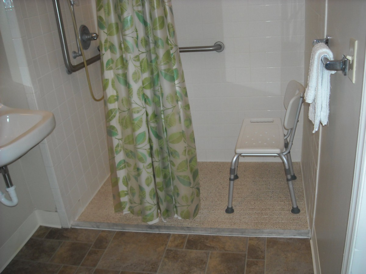 An accessible bathroom with a shower, featuring a safety bar and a chair.