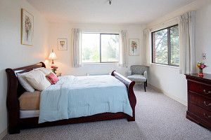 A bright and cozy bedroom with a large bed, windows allowing natural light, and a comfortable chair.