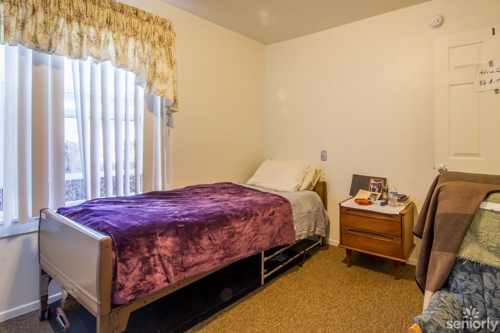 A simple bedroom with a single bed, nightstand, and window with curtains.