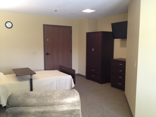A simple and modestly furnished bedroom with a bed, television, and storage furniture.