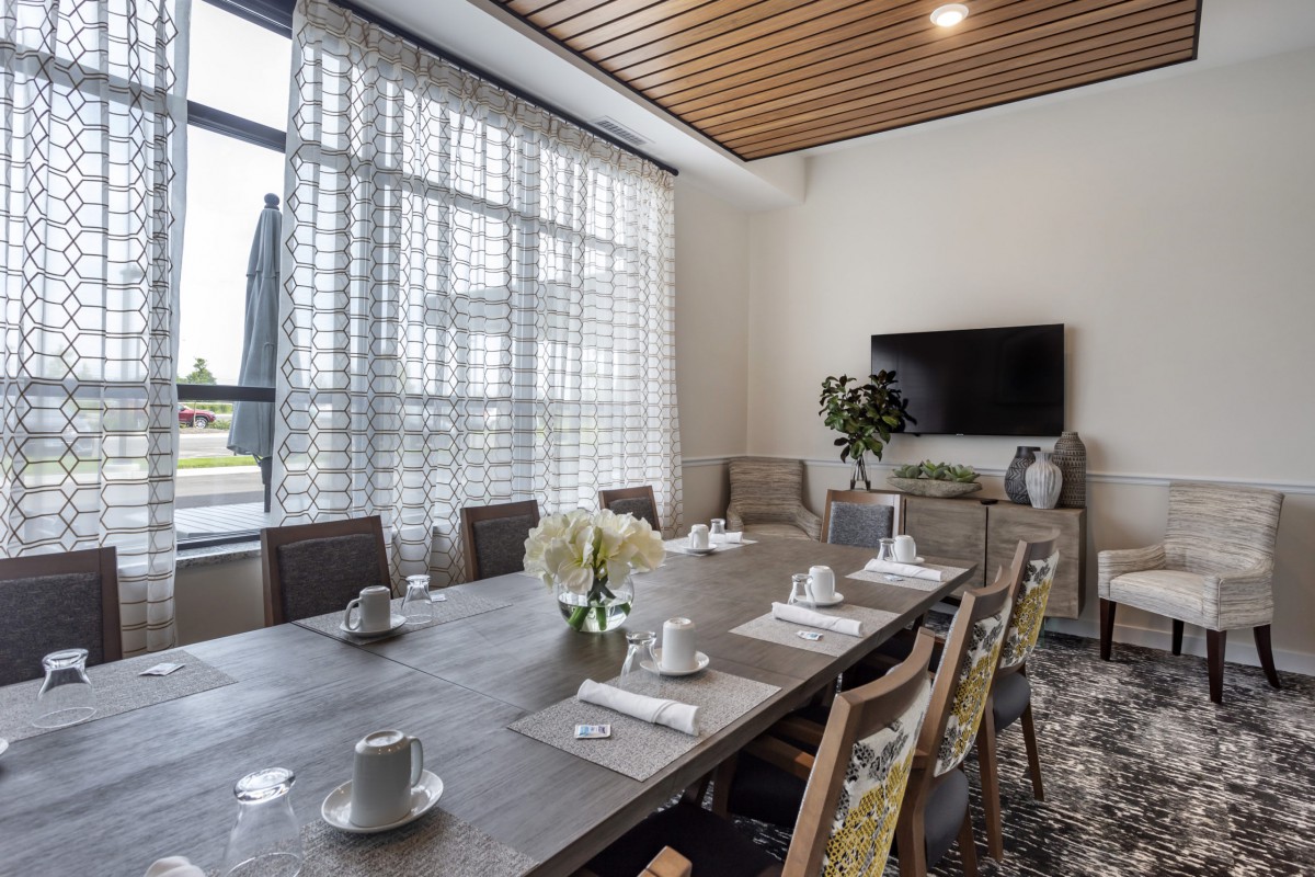 A modern dining room with a large table set for a meeting, featuring elegant decor and natural light from big windows.