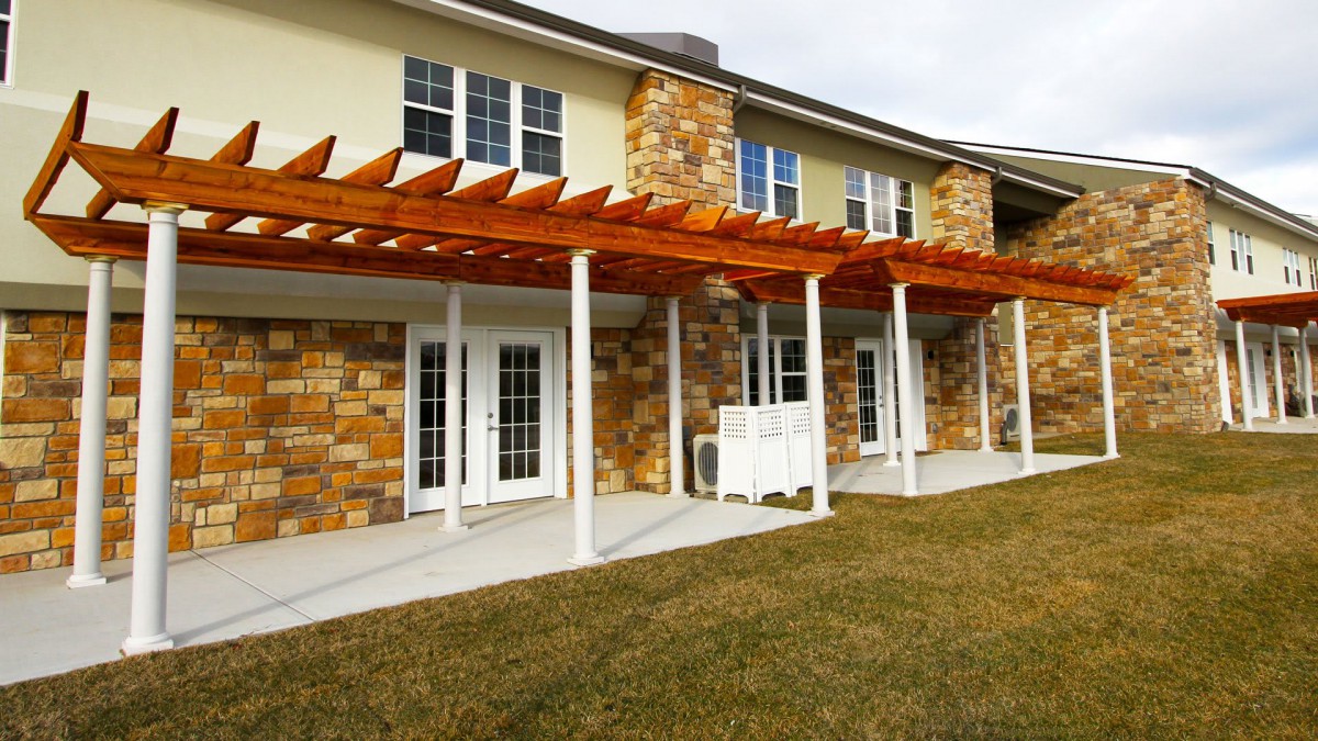 A two-story house with a stone facade and wooden pergola over the patio area.