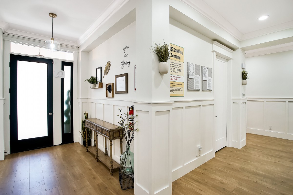 A modern hallway with white walls, wood flooring, and decorative elements such as frames and plants.