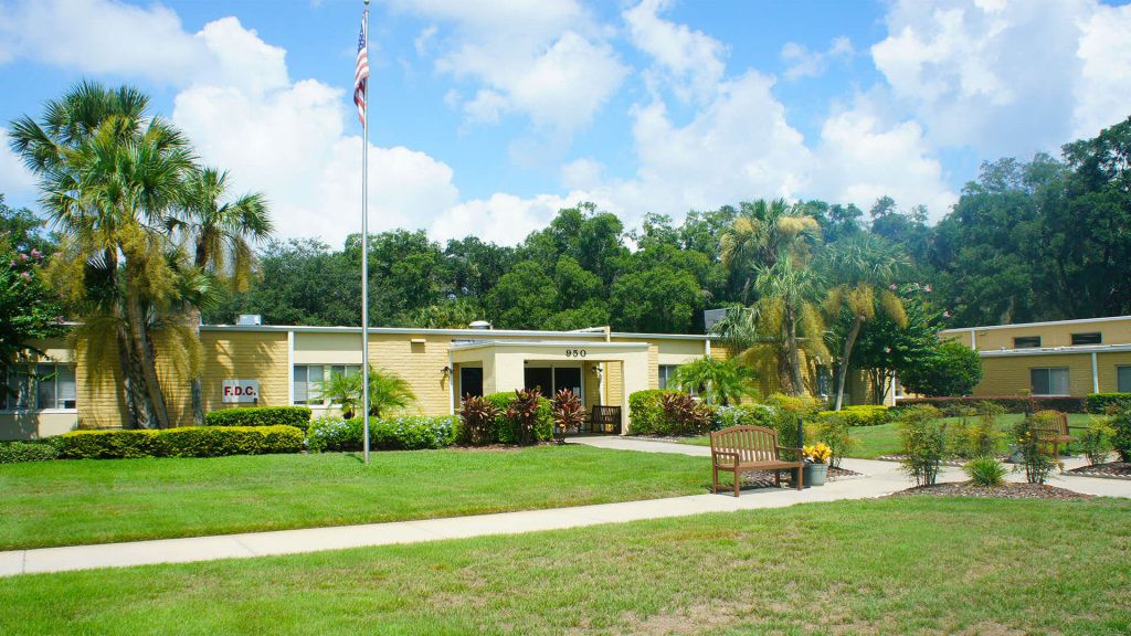 A small building with a flagpole in front, surrounded by grass and trees under a partly cloudy sky.