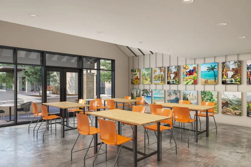 A modern cafe interior with orange chairs and wooden tables, featuring artwork on the walls.