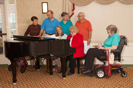 A group of seniors gathered around a piano indoors.