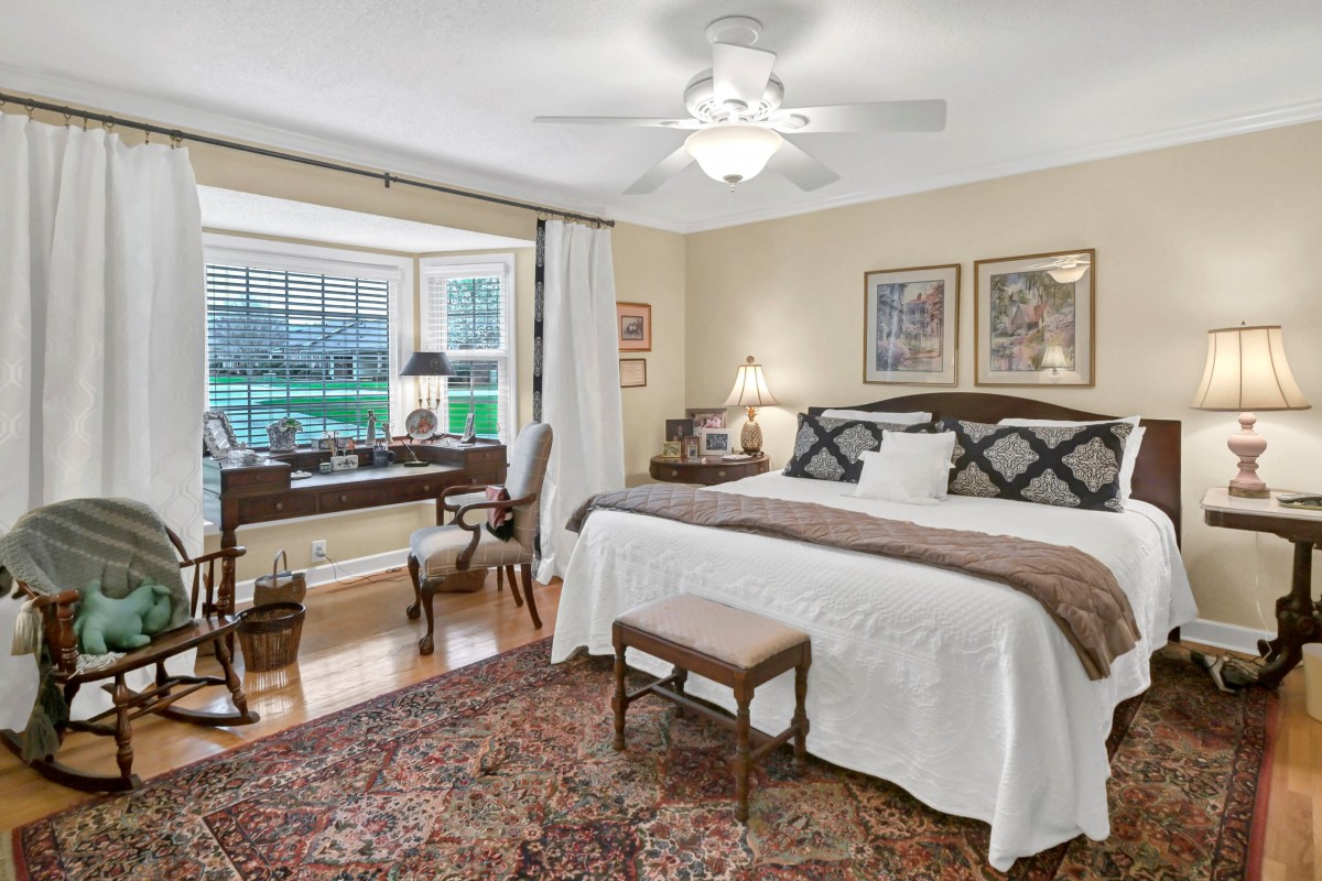 A cozy bedroom with a large bed and a study area by the window, featuring classic decor and warm lighting.