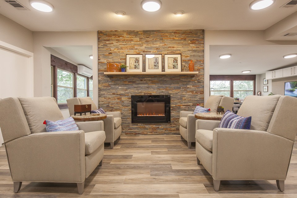 A cozy living room with a modern stone fireplace, flanked by comfortable beige armchairs on wooden flooring.