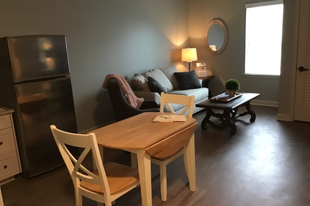A cozy living room with a small wooden dining table, chairs, a comfortable sofa, and ambient lighting.