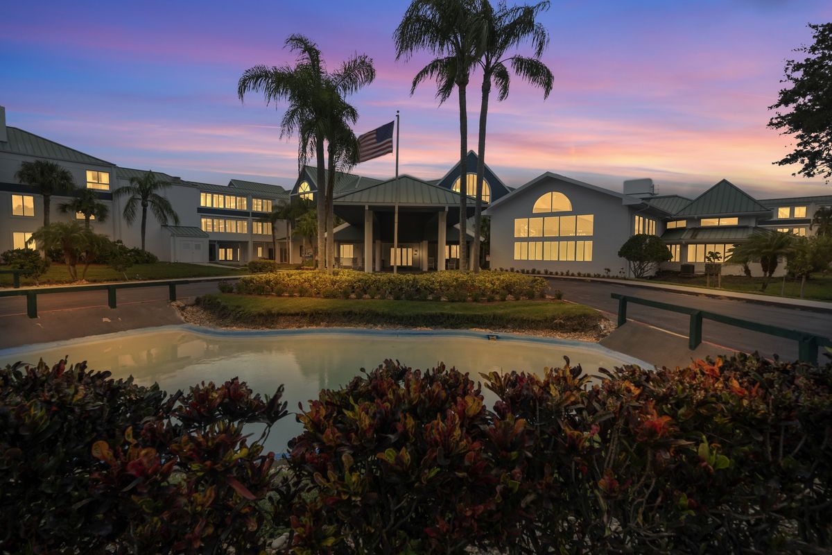 A picturesque view of a resort building at dusk, with palm trees and ambient lighting creating a warm atmosphere.