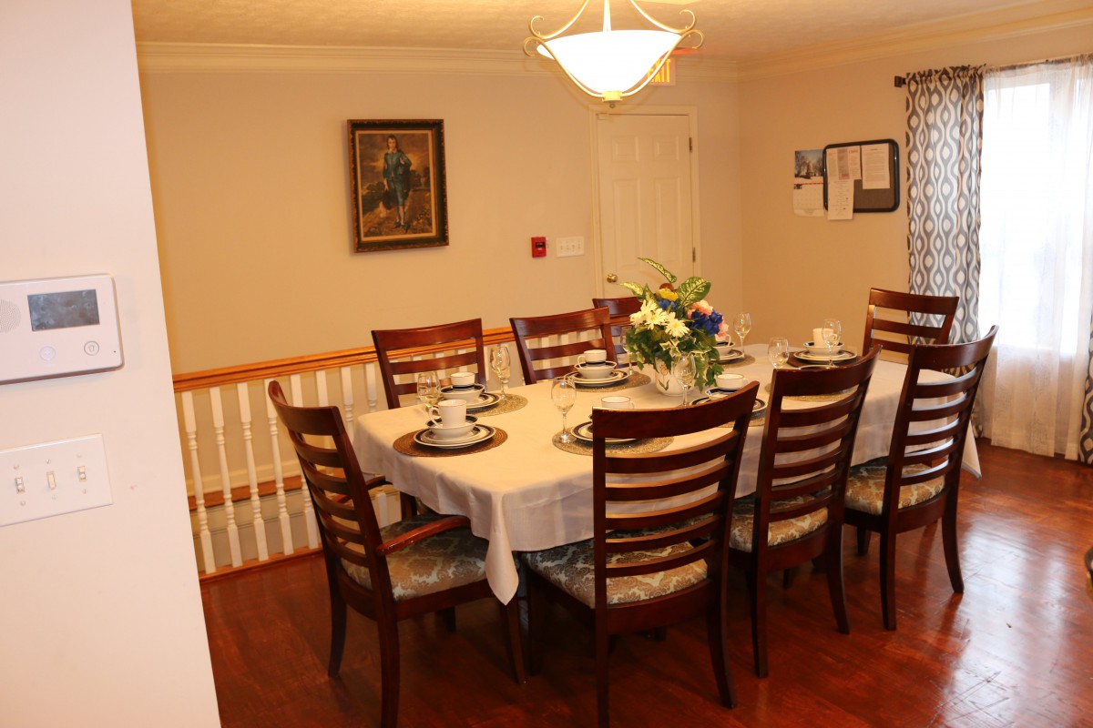 A dining room setup with a wooden table and chairs, adorned with a floral centerpiece under warm lighting.