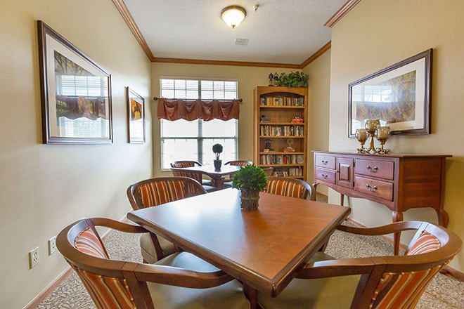 A cozy reading room with a table and chairs, surrounded by bookshelves and adorned with decor.