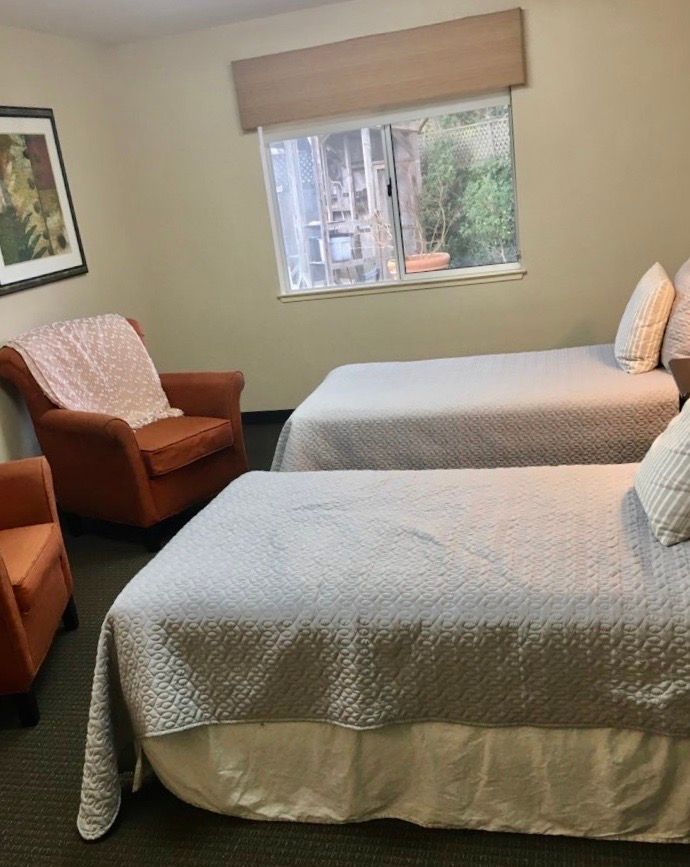 A cozy bedroom featuring two neatly made twin beds and an armchair by the window.