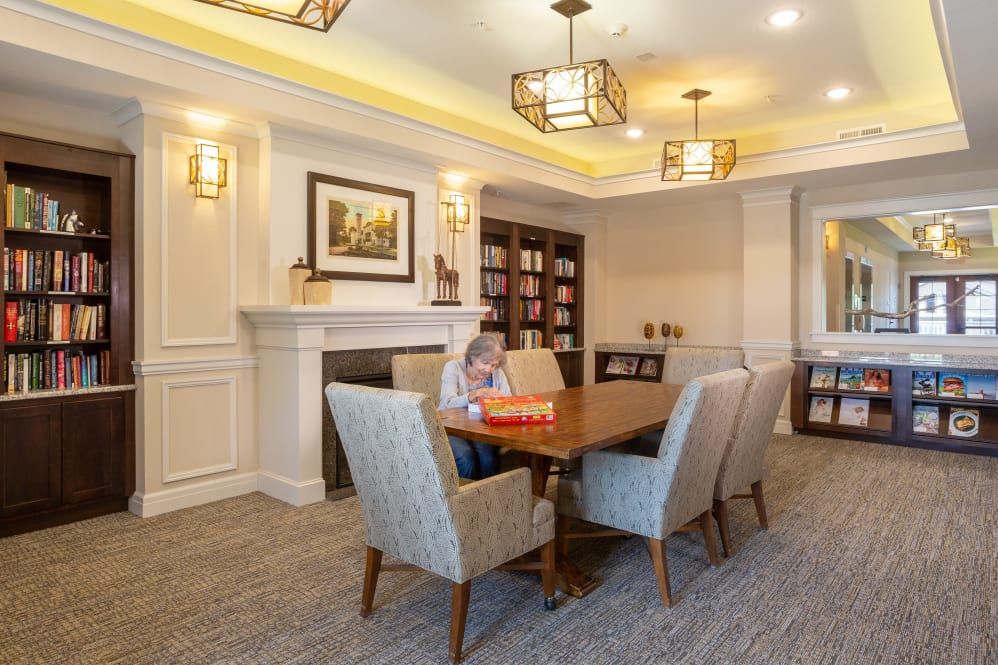 A cozy meeting room with a central table surrounded by chairs, featuring a fireplace and bookshelves.