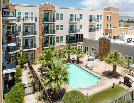 A modern apartment complex featuring a refreshing swimming pool surrounded by palm trees.
