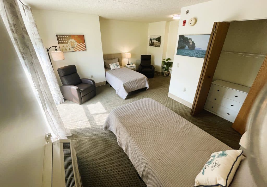 A neatly arranged bedroom with two beds, comfortable chairs, and wall art.