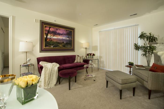 A cozy living room with a burgundy sofa, a painting on the wall, and stylish lighting.