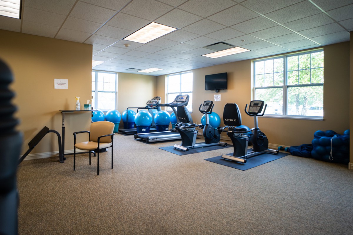 A well-lit gym room featuring treadmills, stationary bikes, and exercise balls.