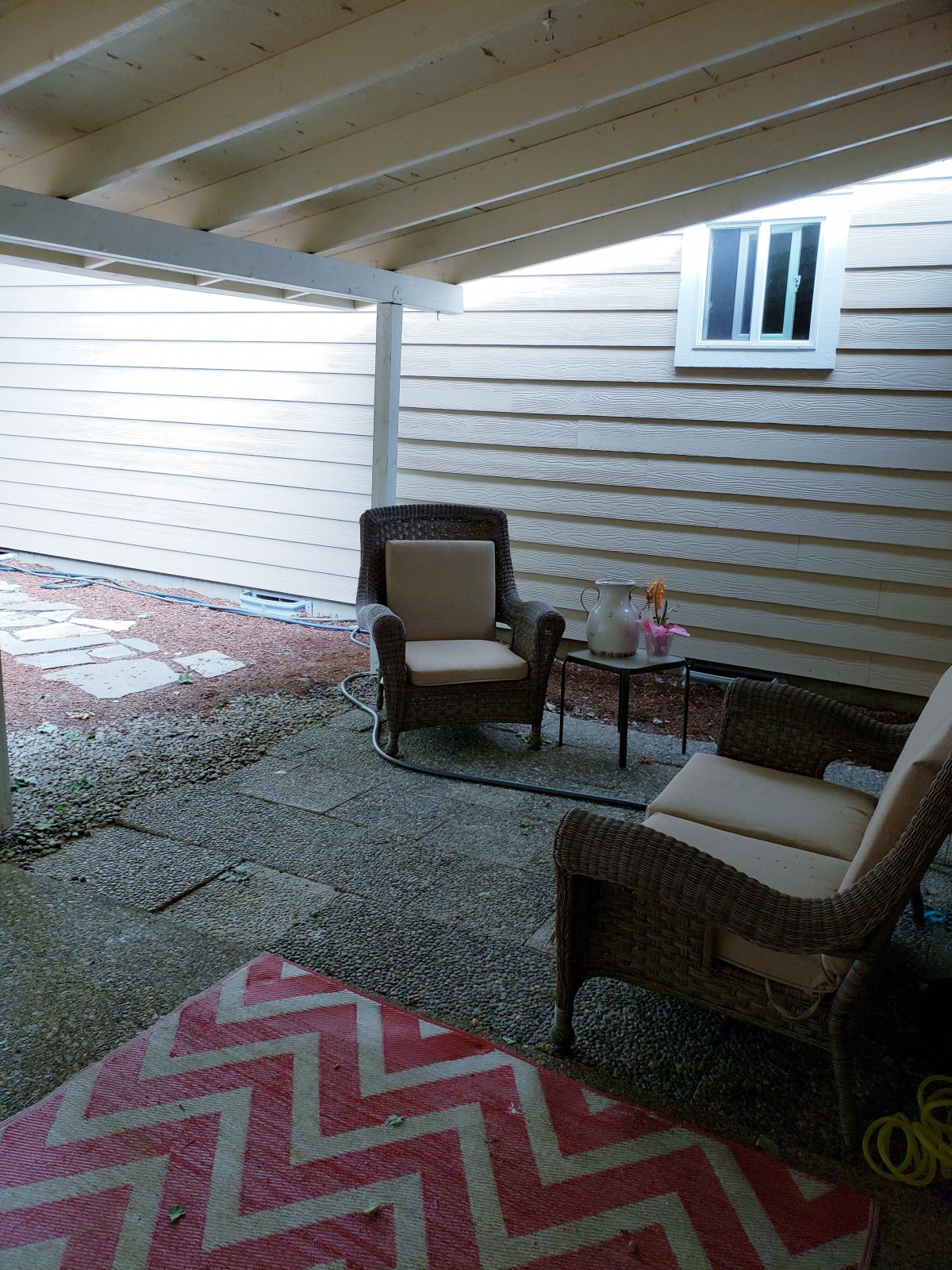 A cozy patio with two chairs, a small table, and a rug under a covered area.