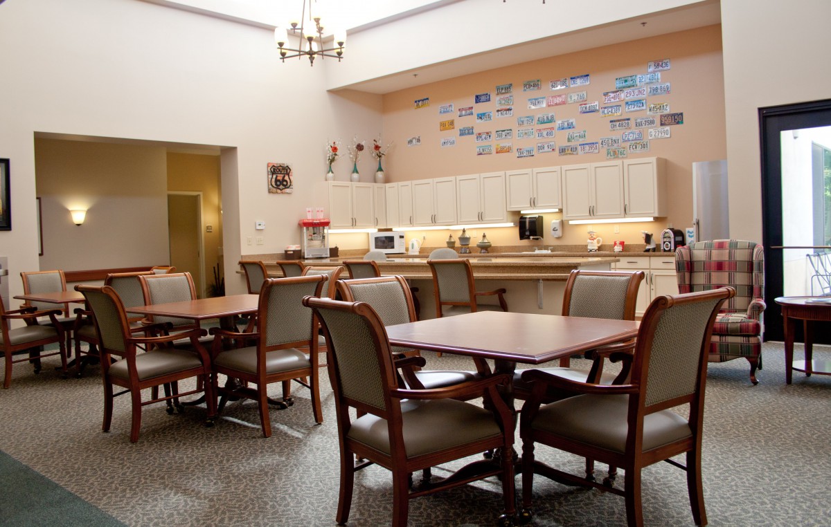 A spacious dining area with tables and chairs, featuring a well-equipped kitchen in the background.
