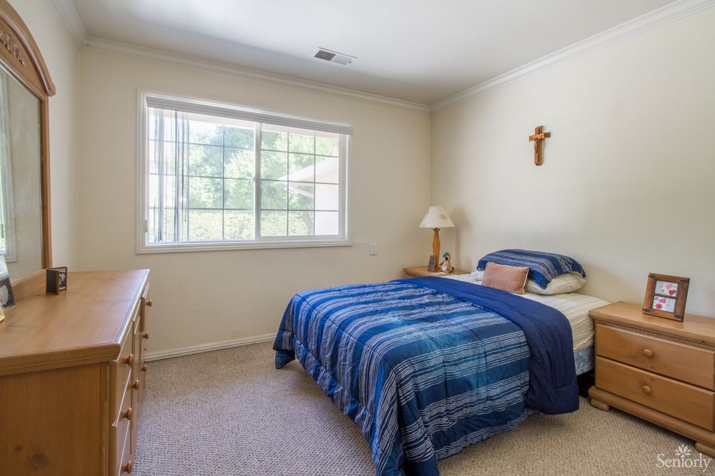 A cozy bedroom with a single bed, blue bedding, and a window letting in natural light.