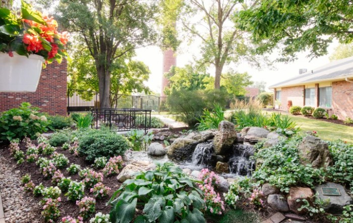 A serene garden featuring a small waterfall, surrounded by lush greenery and colorful flowers.