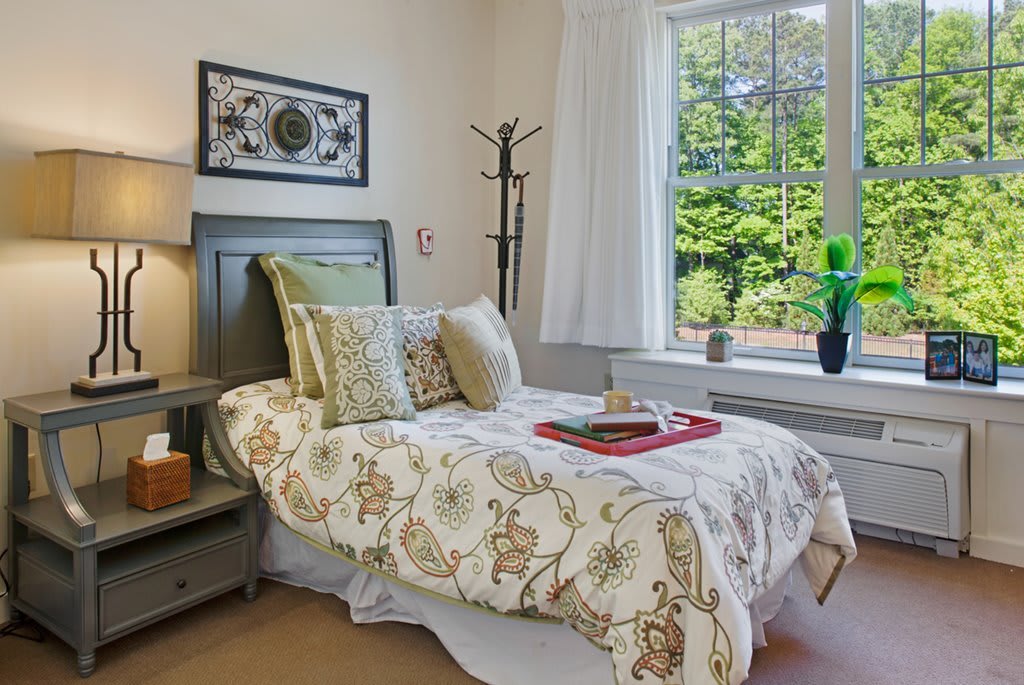 A cozy bedroom with a neatly made bed, decorative pillows, and a window view.
