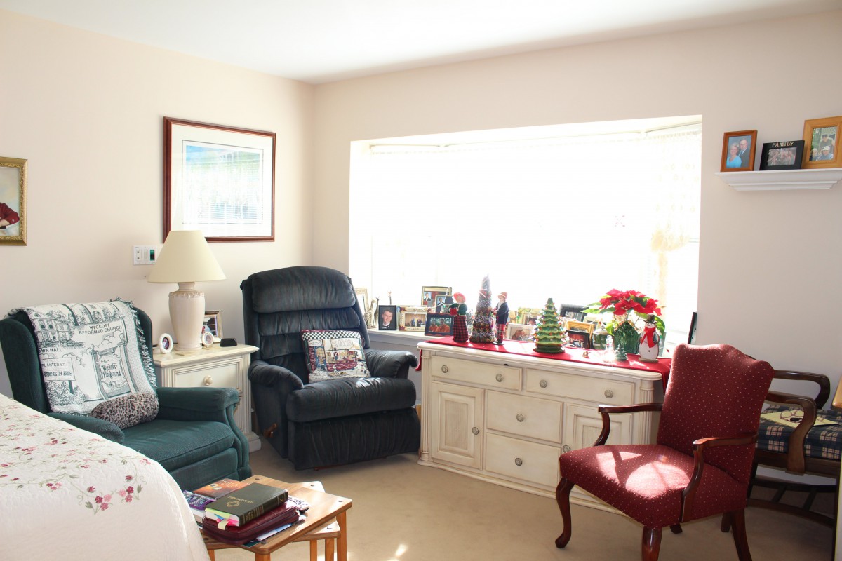 A cozy living room featuring leather recliners, a red armchair, and festive decorations on the dresser under a large window.