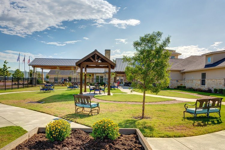 A landscaped garden area with benches and a building in the background on a sunny day.
