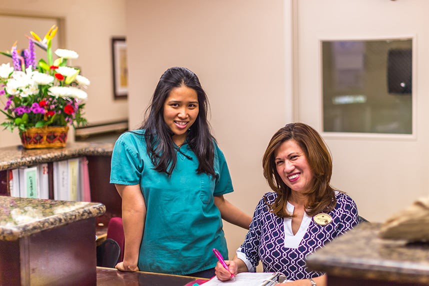 Two women smiling and discussing work in an office setting.