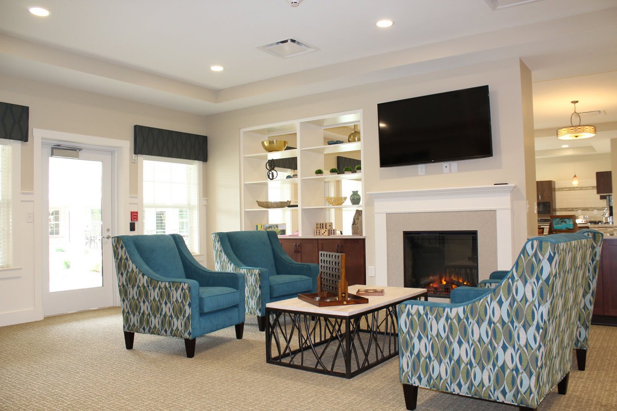 A cozy living room with blue patterned chairs, a fireplace, and a television mounted above it.