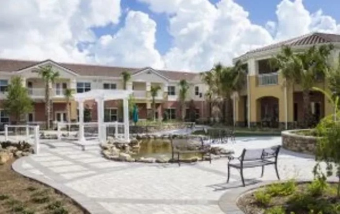 A courtyard with a pond, benches, and surrounding buildings under a partly cloudy sky.