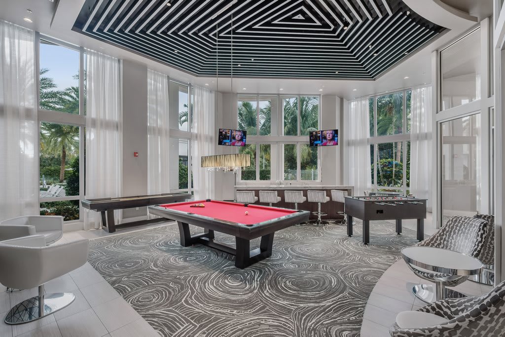 A modern game room featuring a pool table with bright natural lighting from large windows.