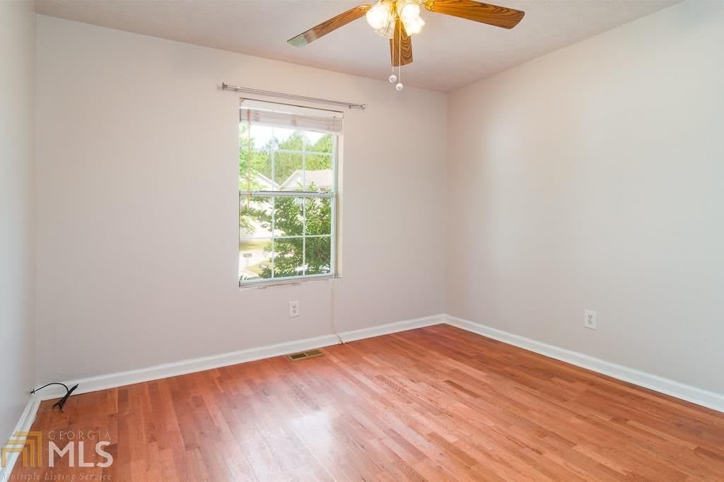 An empty room with hardwood flooring, a ceiling fan, and a window letting in natural light.