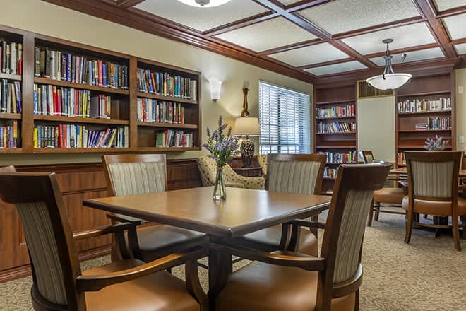 A cozy library reading room with bookshelves, a wooden table, and chairs.