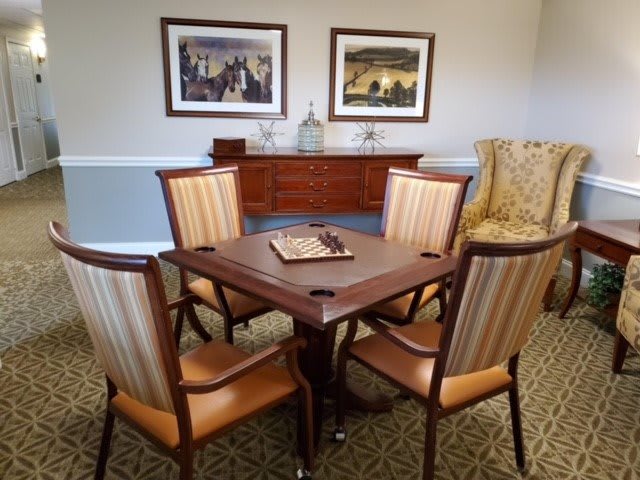 A well-furnished living room with a table set for a board game, surrounded by four chairs and decorated with artwork on the walls.