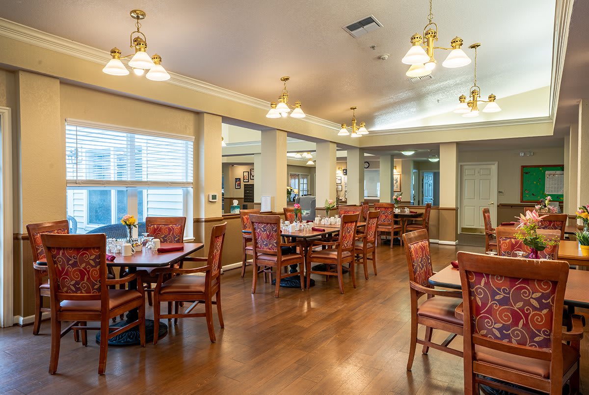 A spacious dining room with neatly arranged tables and chairs, warm lighting, and wood flooring.