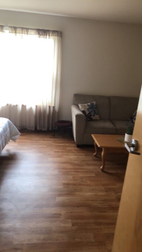 A cozy room with a bed, couch, and wooden flooring.