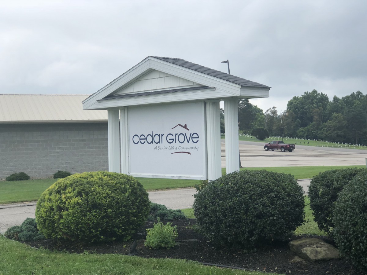 A roadside sign displaying 'Cedar Grove' surrounded by well-maintained bushes.
