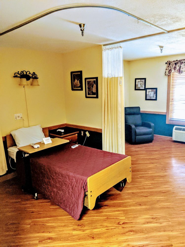 A tidy hospital room with a bed, side table, and a comfortable chair.