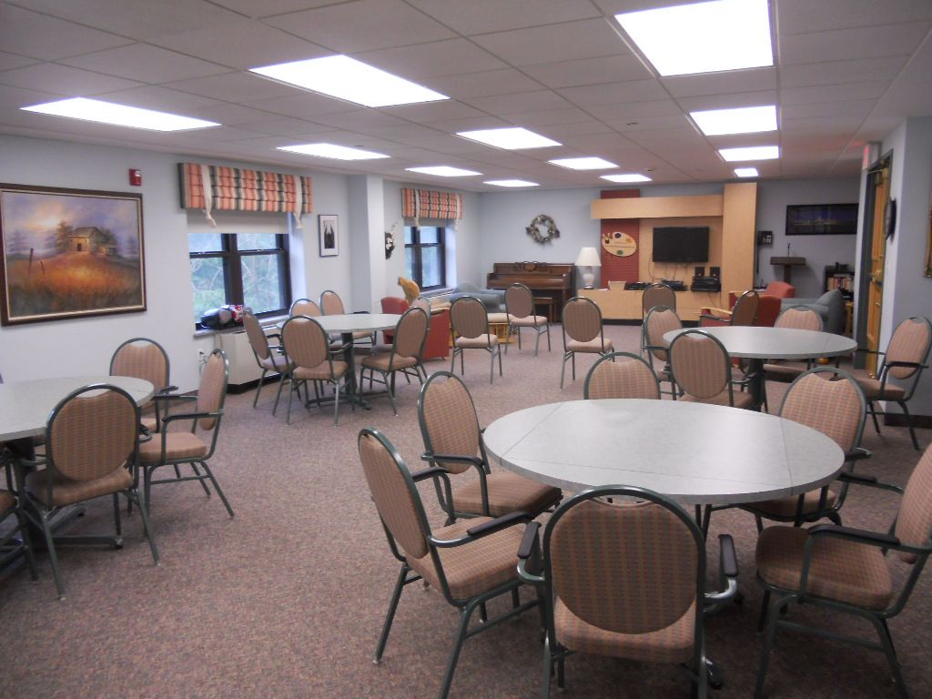 A spacious community room with multiple tables and chairs, well-lit with natural and artificial lighting.