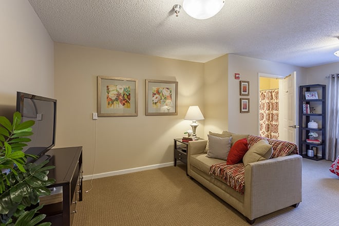 A cozy living room with a sofa, side table, lamp, and framed artwork on the walls.