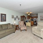 A cozy living room with an open layout leading to the kitchen, featuring a sofa, armchair, and various decorations.