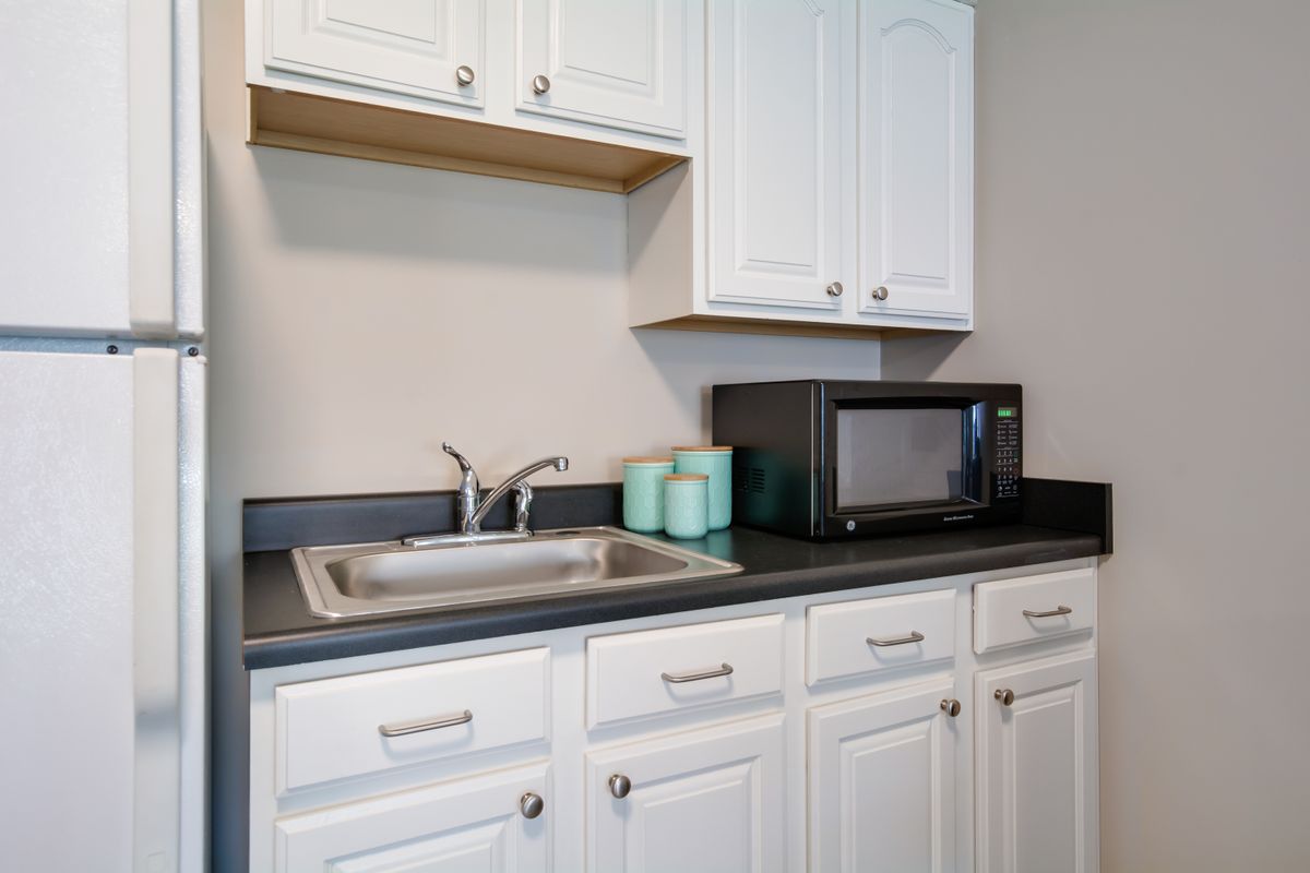 A small kitchen area with white cabinets, a sink, and a microwave on the countertop.