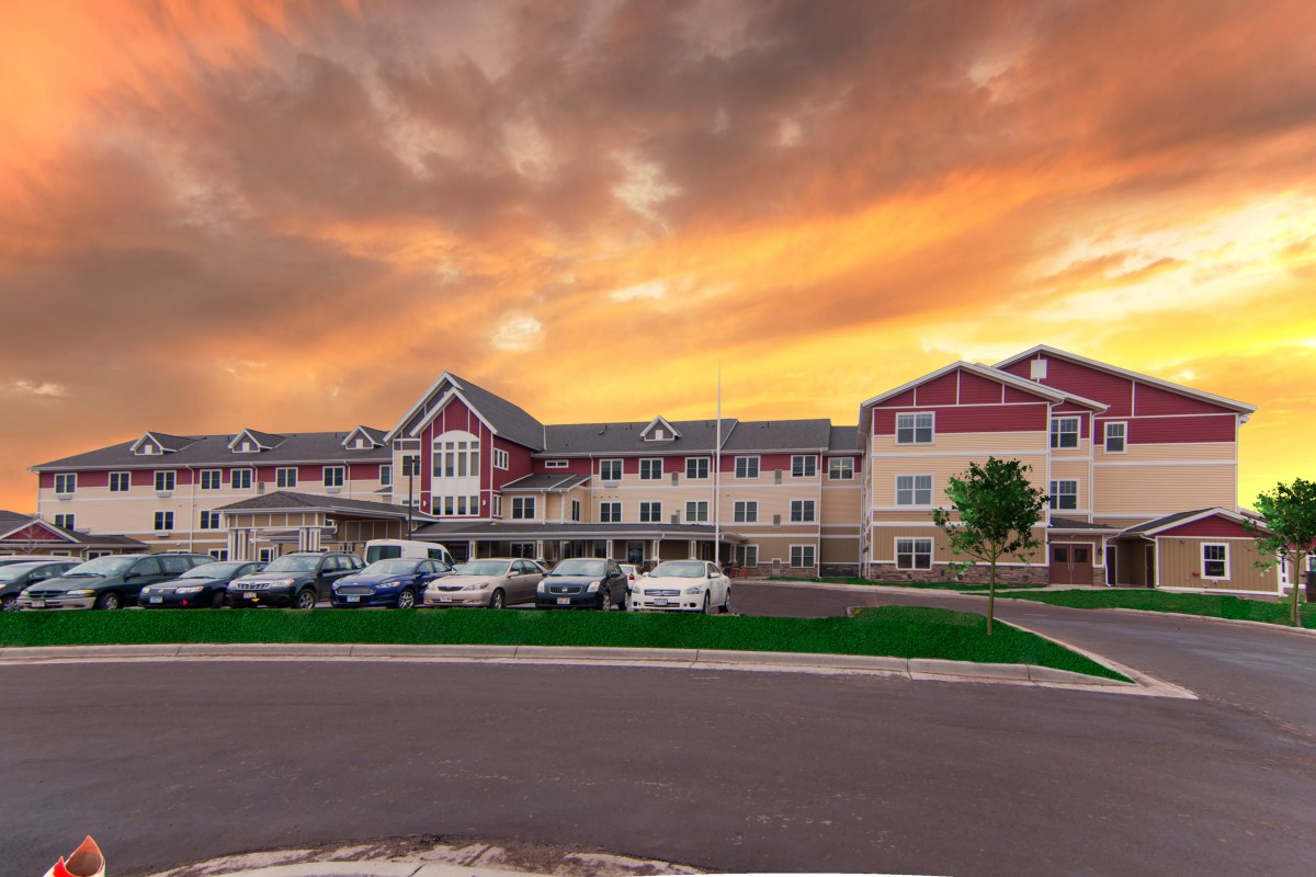 A residential building with a parking lot in front, set against a dramatic sunset sky.