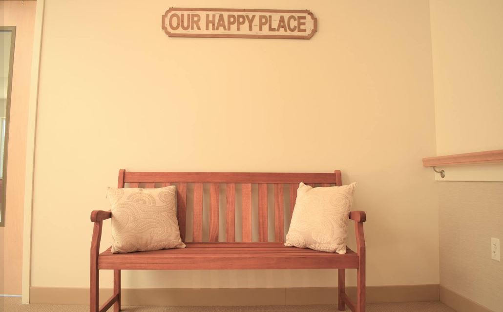 A cozy wooden bench with two pillows beneath a sign that reads 'Our Happy Place'.