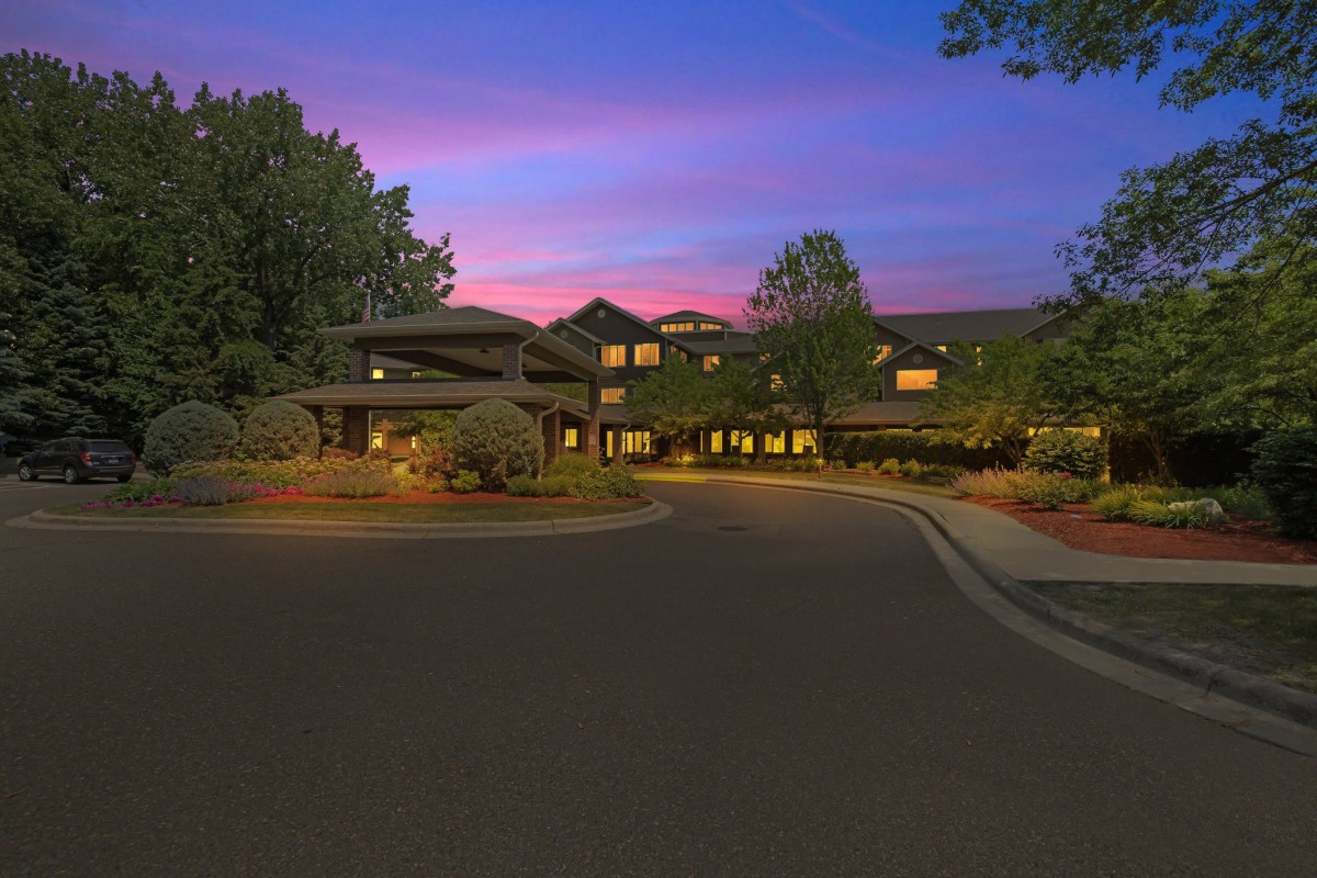 A building surrounded by trees at twilight with a winding road leading to its entrance.