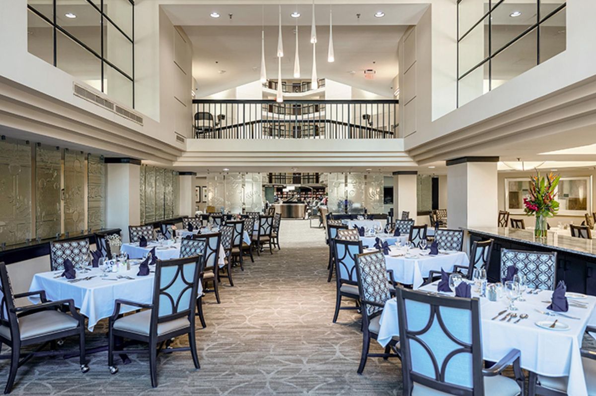 A spacious and elegantly designed restaurant interior with neatly arranged tables and chairs, complemented by modern chandeliers.
