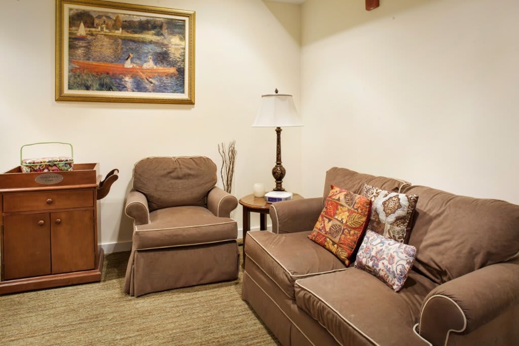 A cozy living room with a comfortable sofa and armchair, decorated with colorful cushions and a stylish lamp beside a framed artwork.
