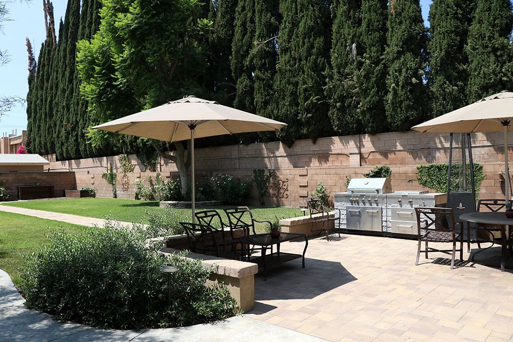 A well-maintained backyard with a patio featuring outdoor seating, a large umbrella, and a grill area.
